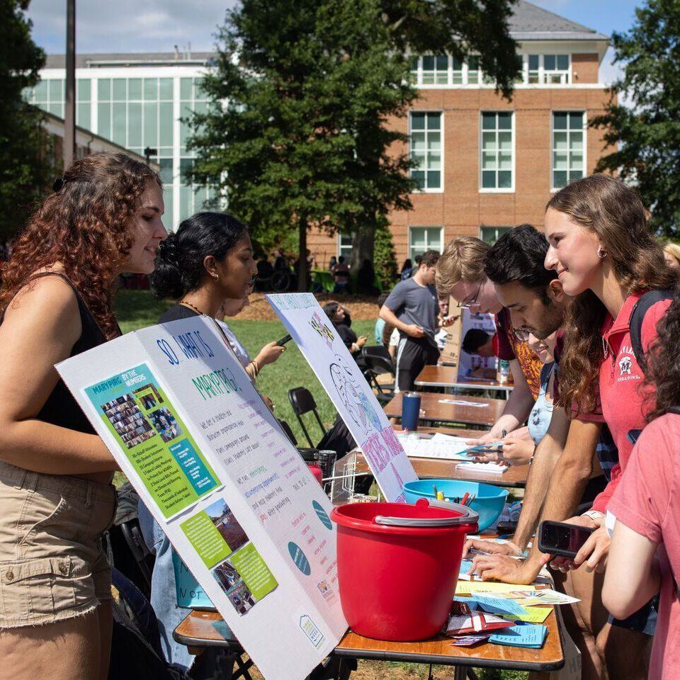 Groups of students outside at standing at tables with poster displays reviewing organization types.